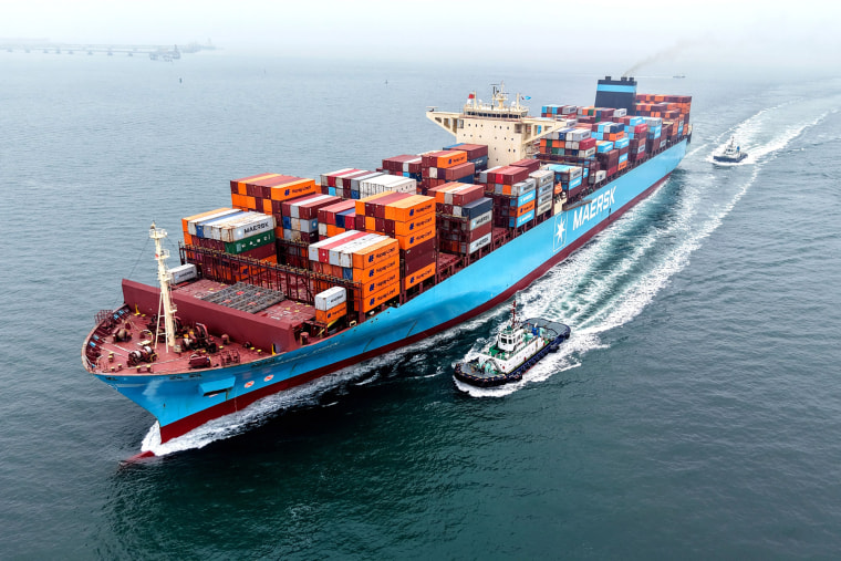 A cargo ship loaded with foreign trade containers sails on the water next to smaller boats