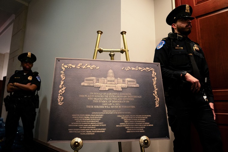 Two Capitol police officers stand on either side of a large metal plaque on display in a hallway.