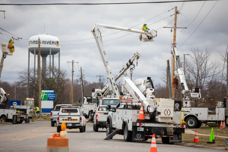 Utility workers in crane baskets work on power lines.