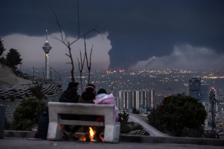 People watch smoke plumes in the distance on the skyline