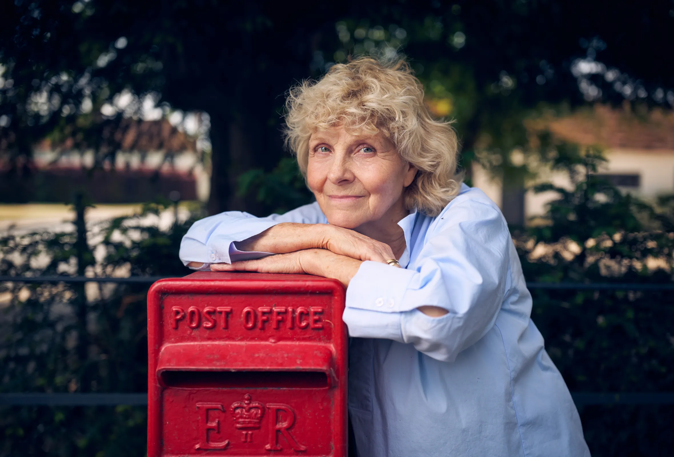 Jo Hamilton, victim of the Post Office scandal, leaning on a red Post Office box.