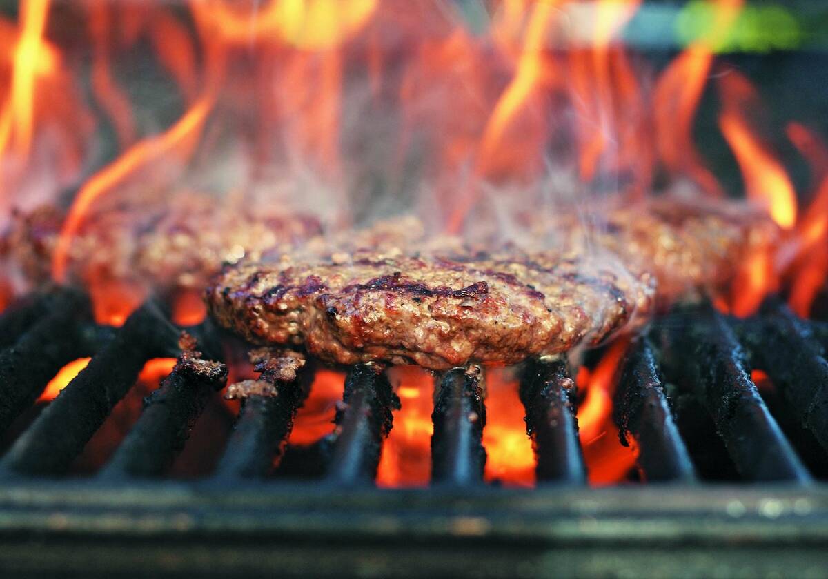 Flames rise up around a burger cooking on a grill.