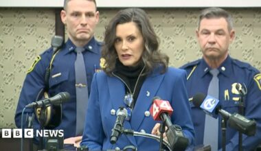 A woman with dark hair and a multiple colour jumper siting on a green sofa inside her living room.