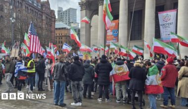 Crowds of people fly a version of the Iranian flag with a historic Persian symbol along with some US and Israeli flags