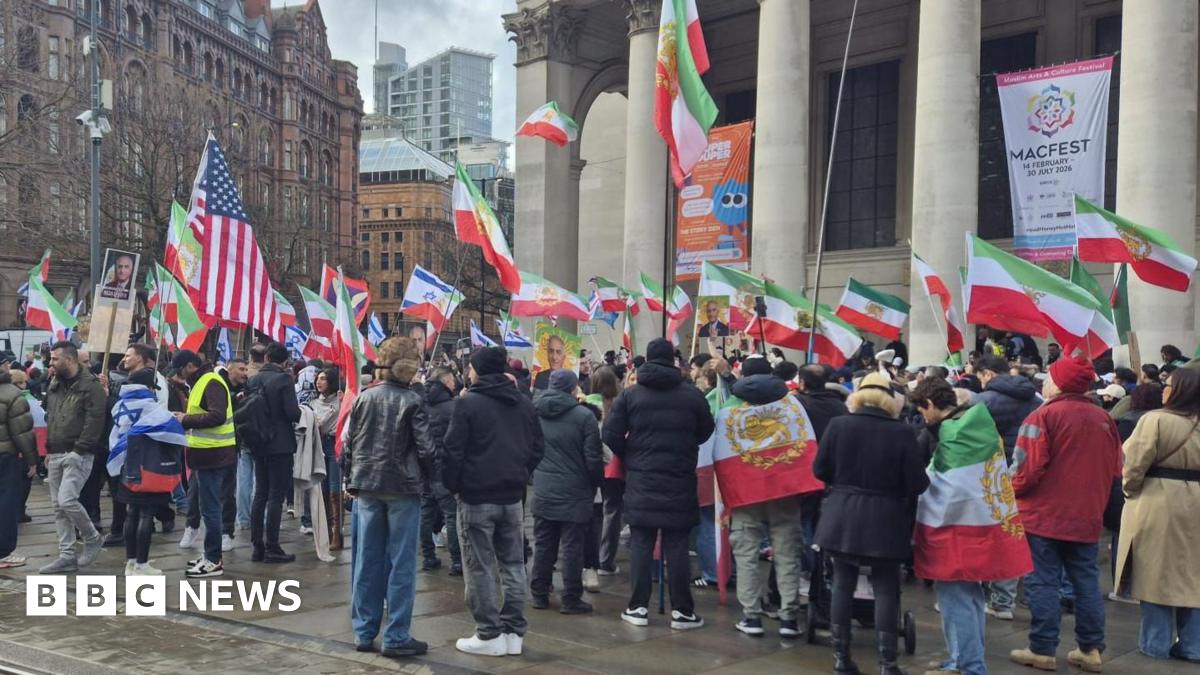 Crowds of people fly a version of the Iranian flag with a historic Persian symbol along with some US and Israeli flags