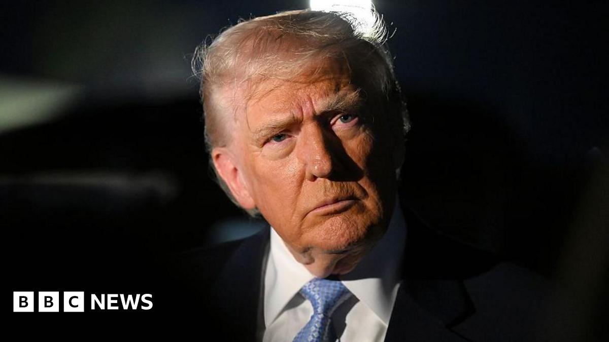 Trump wearing a black suit and blue tie looks into the distance. The background is black.