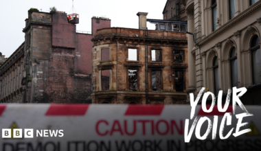 Shell of a fire damaged Victorian building. A red and white barrier warning that demolition is in progress is in the foreground.