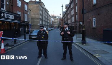 Two police officers stand behind a police cordon on a street in London