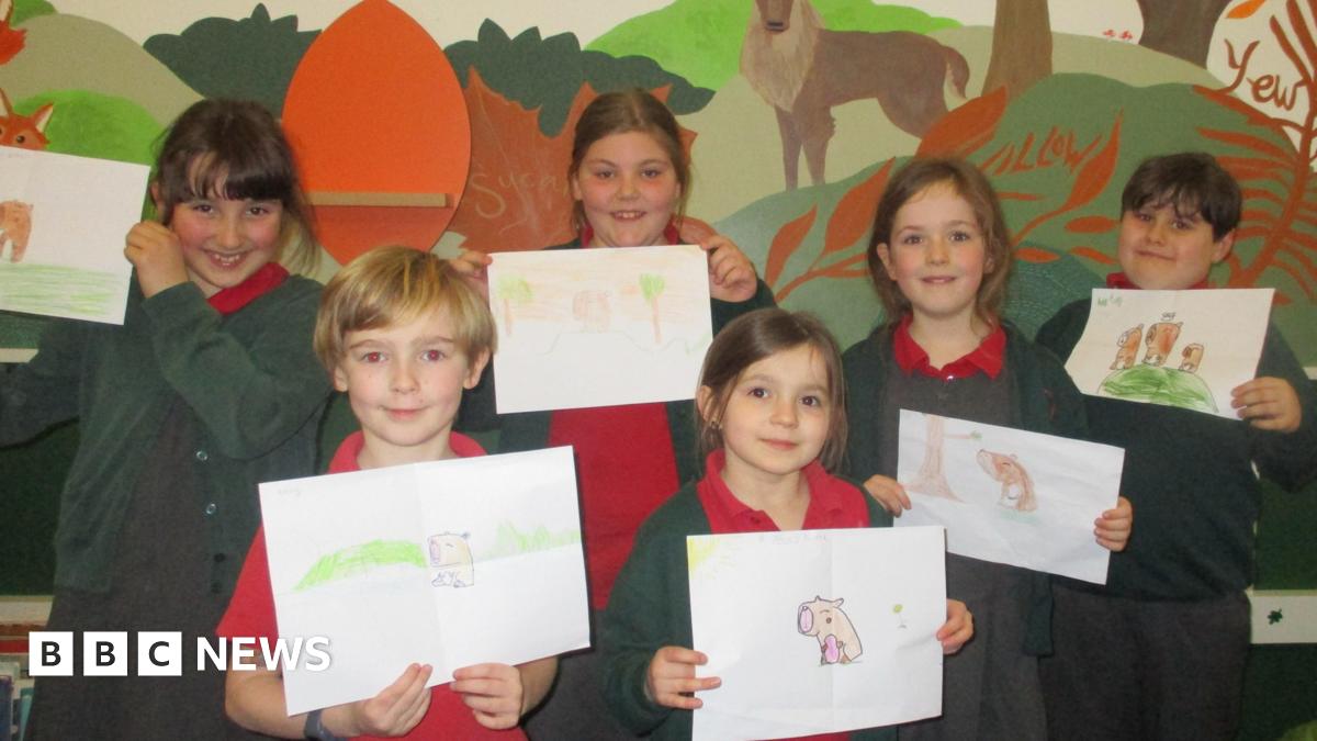 A group of schoolchildren wearing uniform hold up drawings of capybaras.