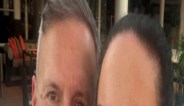 Laura and Paul Webster, a man with shirt grey hair and a mustache is wearing a white tshirt and looking at the camera with a slight smile, a woman next to him has dark brown hair pulled back and pearl earrings and looking at the camera with a wide smile