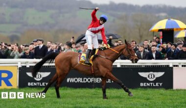 A woman with dark hair and a multiple colour jumper siting on a green sofa inside her living room.