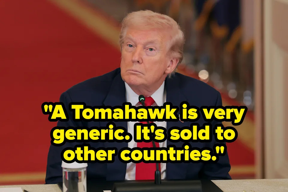 A person in a suit with a red tie sits at a table, facing forward, during a formal meeting