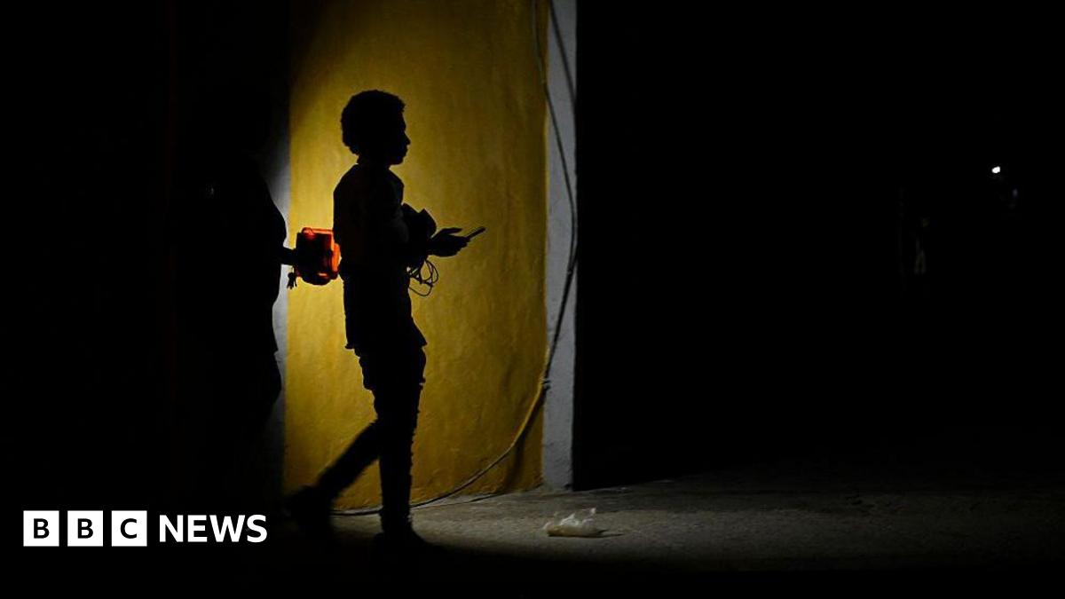 Two people holding a flashlight while walking on a dark street.