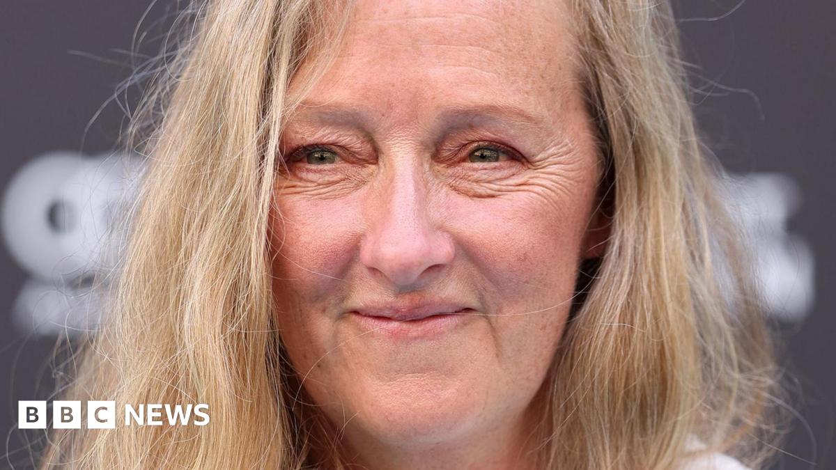 A close up of a middle-aged woman with long blonde hair, smiling at the camera.