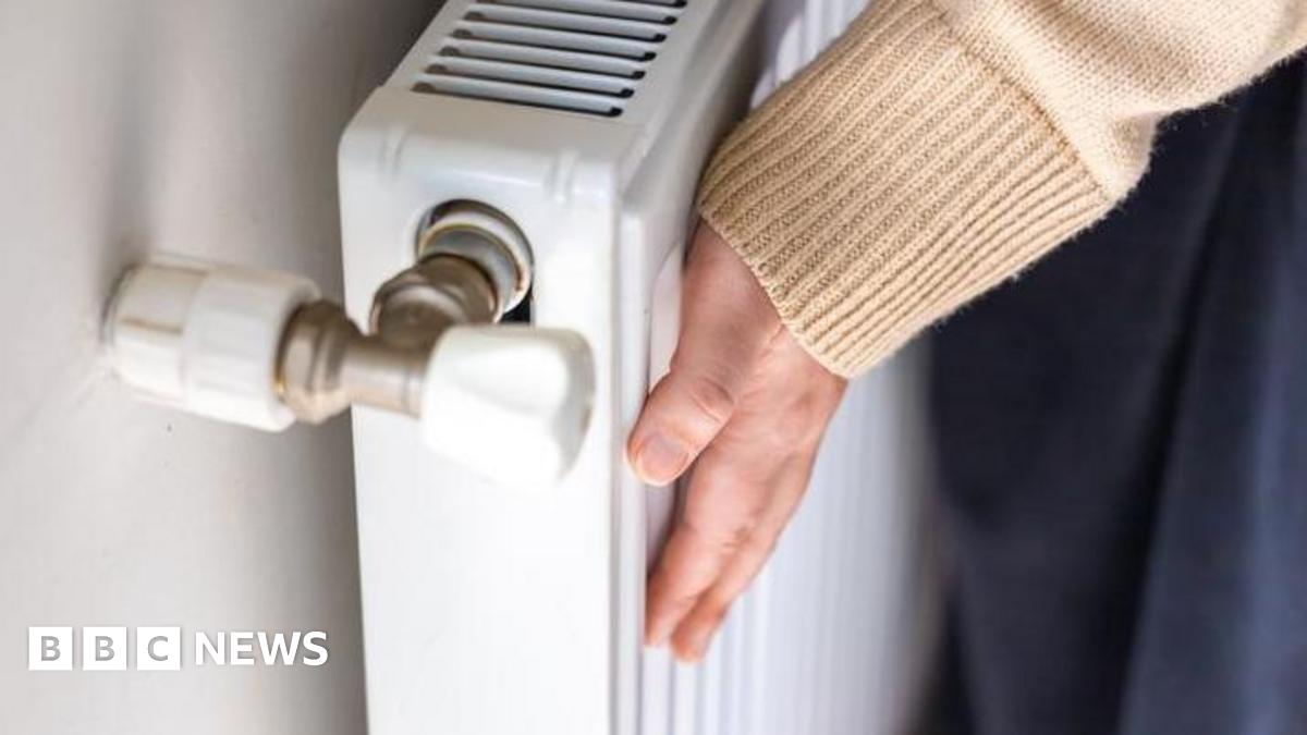 A woman touches a radiator in a house to check how warm it is. She is wearing a beige jumper. The close-up picture shows her hand and sleeve.