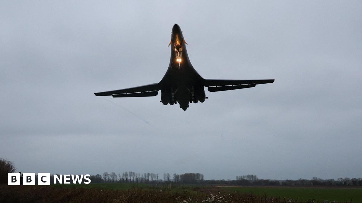 A large bomber aircraft is pictured with a bright light shining as it approaches a runway at an airbase.
