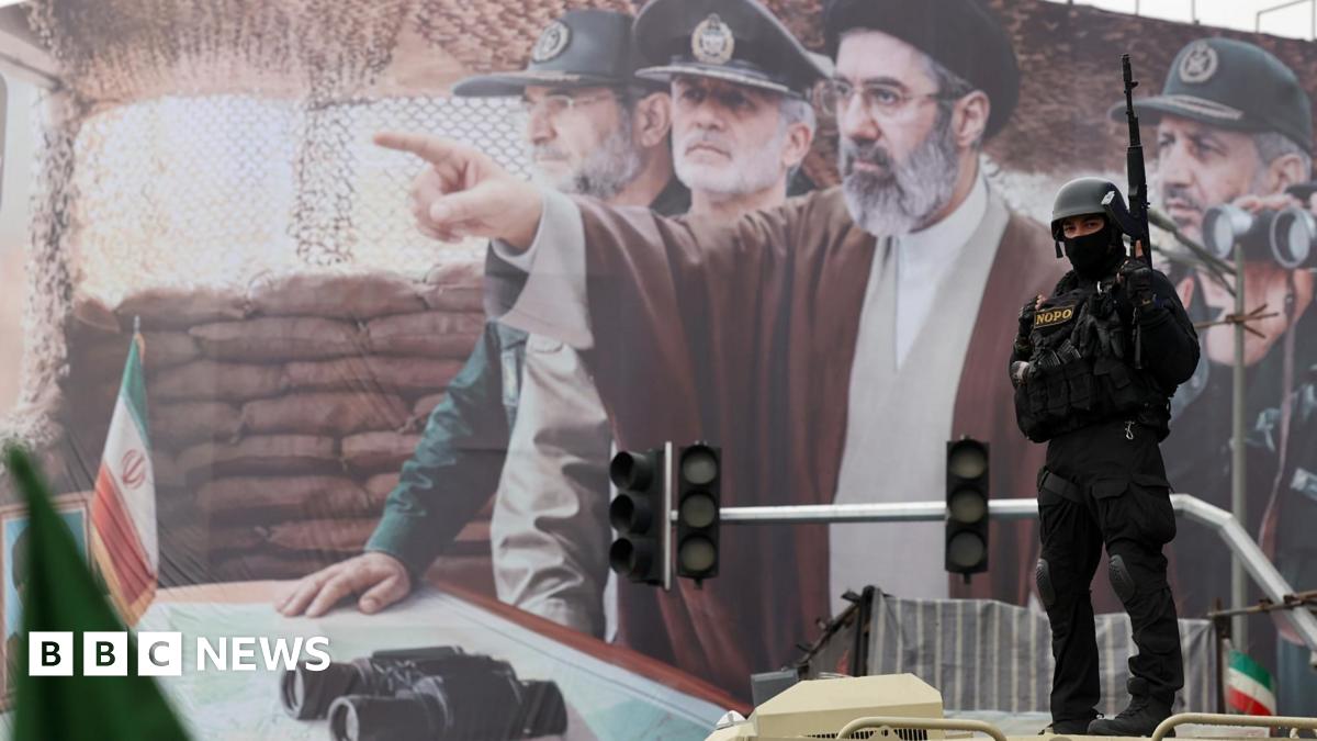 A woman with dark hair and a multiple colour jumper siting on a green sofa inside her living room.