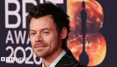 A woman with dark hair and a multiple colour jumper siting on a green sofa inside her living room.