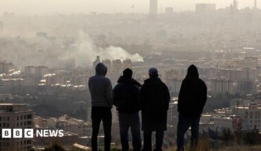 Men watch from a hillside as a plume of smoke rises after an explosion on 2 March 2026 in Tehran, Iran.