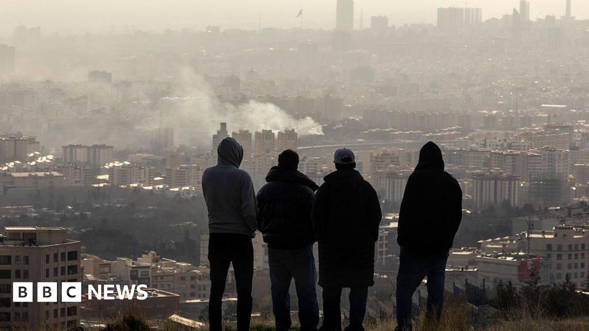 Men watch from a hillside as a plume of smoke rises after an explosion on 2 March 2026 in Tehran, Iran.