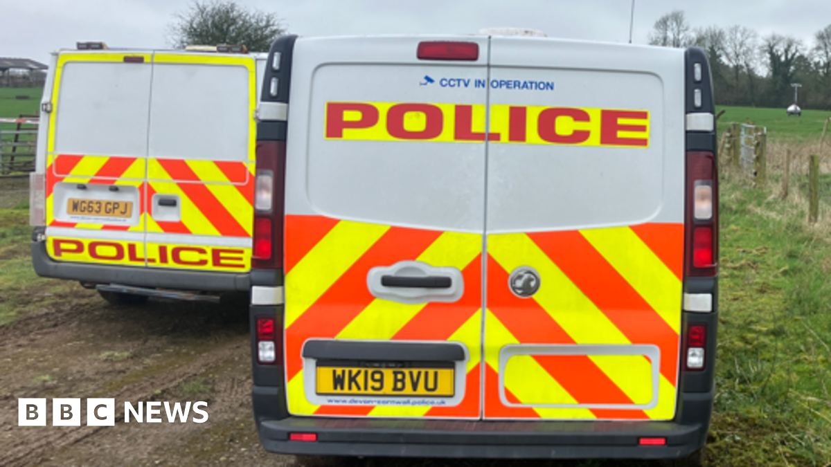 Two police vans on a driveway at Dunkeswell Aerodrome. There is a grass field with a red tent in background.