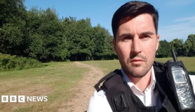 Handout photo issued by the Crown Prosecution Service of Ryan Connolly who is wearing a police uniform of white shirt and a black vest which has a communication device attached to it. He has straight dark hair, brushed into a side parting and has slight facial stubble. He looks directly into the camera, behind him a wide open space of grass is visible, with a path worn into it. Beyond that are trees in leaf and a bright blue sky