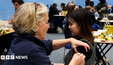 A nurse administering a vaccine to a woman sat in a black chair next to her.