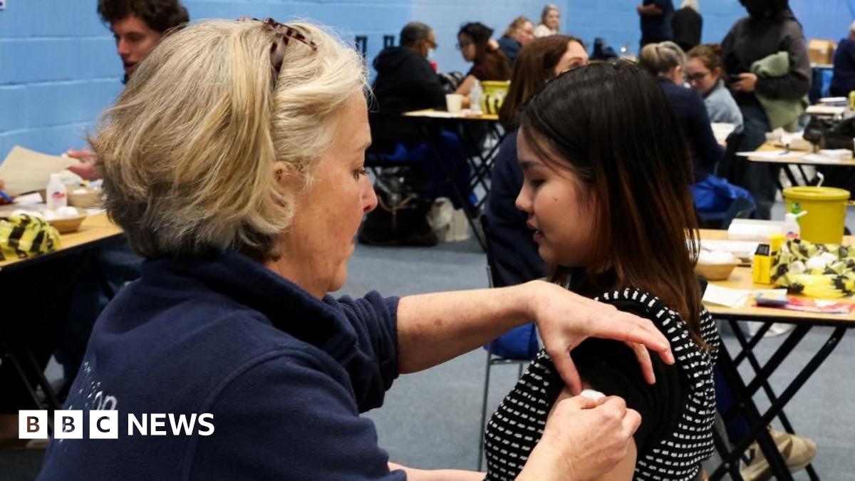 A nurse administering a vaccine to a woman sat in a black chair next to her.