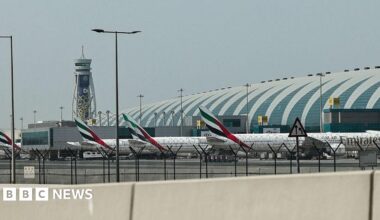 Three Emirates planes lined up at Dubai International Airport, a control tower stands in the background.