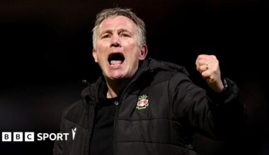 Phil Parkinson in a black Wrexham coat celebrates with a punch in the air