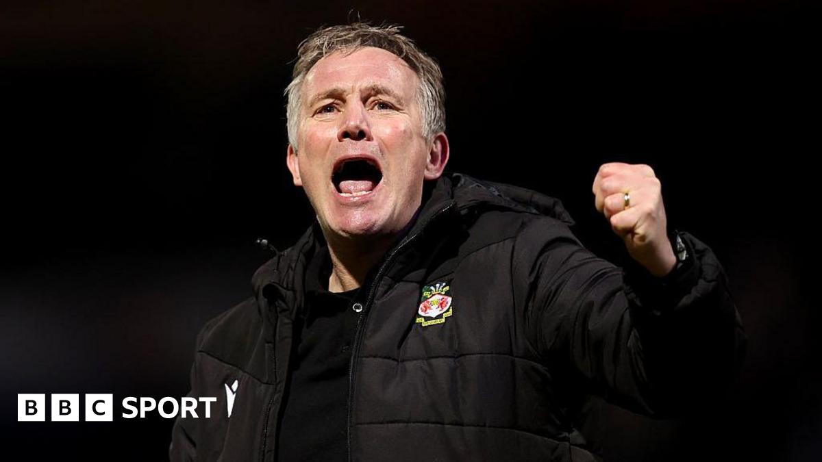 Phil Parkinson in a black Wrexham coat celebrates with a punch in the air