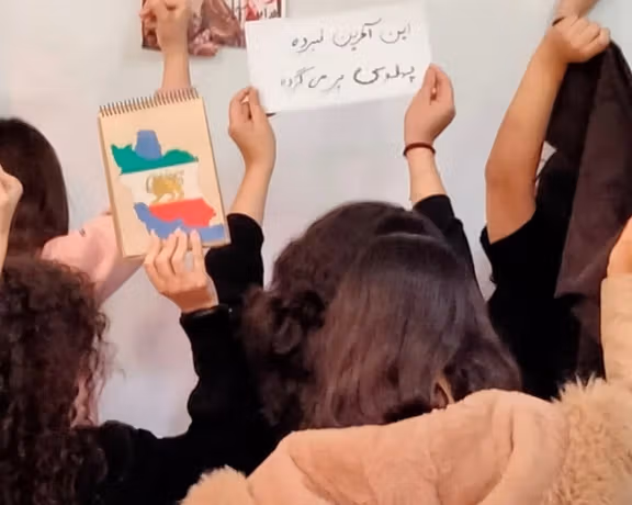 Schoolgirls in Iran raise fists in protest; a handwritten sign reads, “This is the final battle, Pahlavi will return.” (Undated)