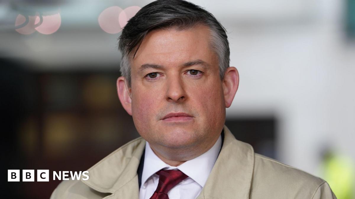 Jonathan Ashworth wearing shirt and tie and a cream coat