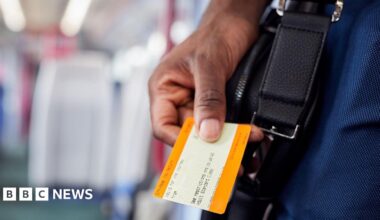 A hand holds a UK rail ticket.