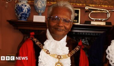 Dr Bharat Pankhania. He has short grey hair and glasses and is wearing civic regalia. He is looking at the camera and smiling.
