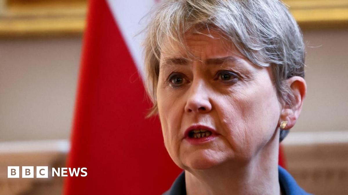 Foreign Secretary Yvette Cooper is speaking and stood in front of a flag. She is wearing a blue jacket.