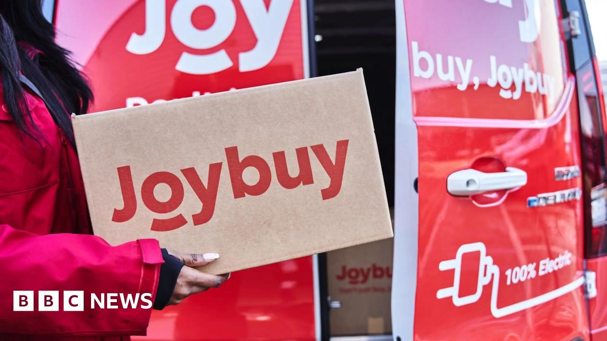 A woman in a red coat is carrying a cardboard box with "Joybuy" printed in red letters. Behind is a red van with a door partially open showing boxes in the back of it.