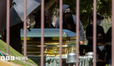 Mourners - some of them wearing surgical masks - look on as a gold-coloured casket containing the body of cartel leader Nemesio Oseguera Cervantes, known as "El Mencho," is displayed during his funeral at the Recinto de la Paz cemetery in Zapopan, Mexico,  on 2 March, 2026.