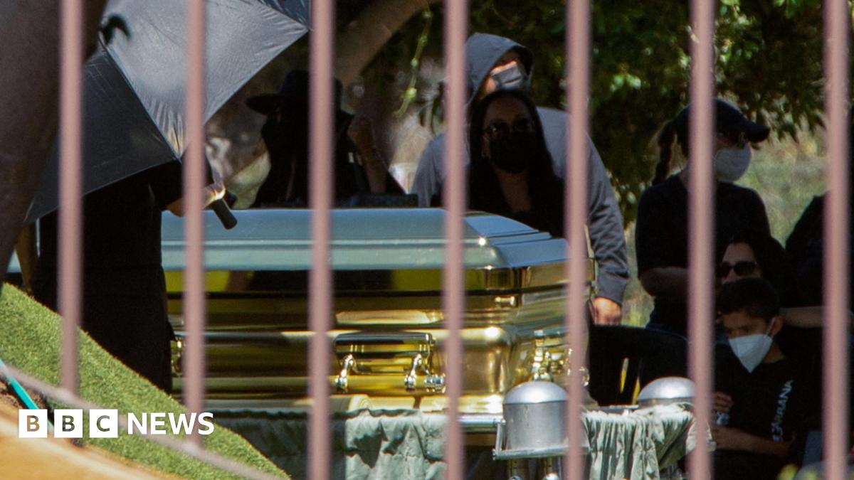 Mourners - some of them wearing surgical masks - look on as a gold-coloured casket containing the body of cartel leader Nemesio Oseguera Cervantes, known as "El Mencho," is displayed during his funeral at the Recinto de la Paz cemetery in Zapopan, Mexico,  on 2 March, 2026.