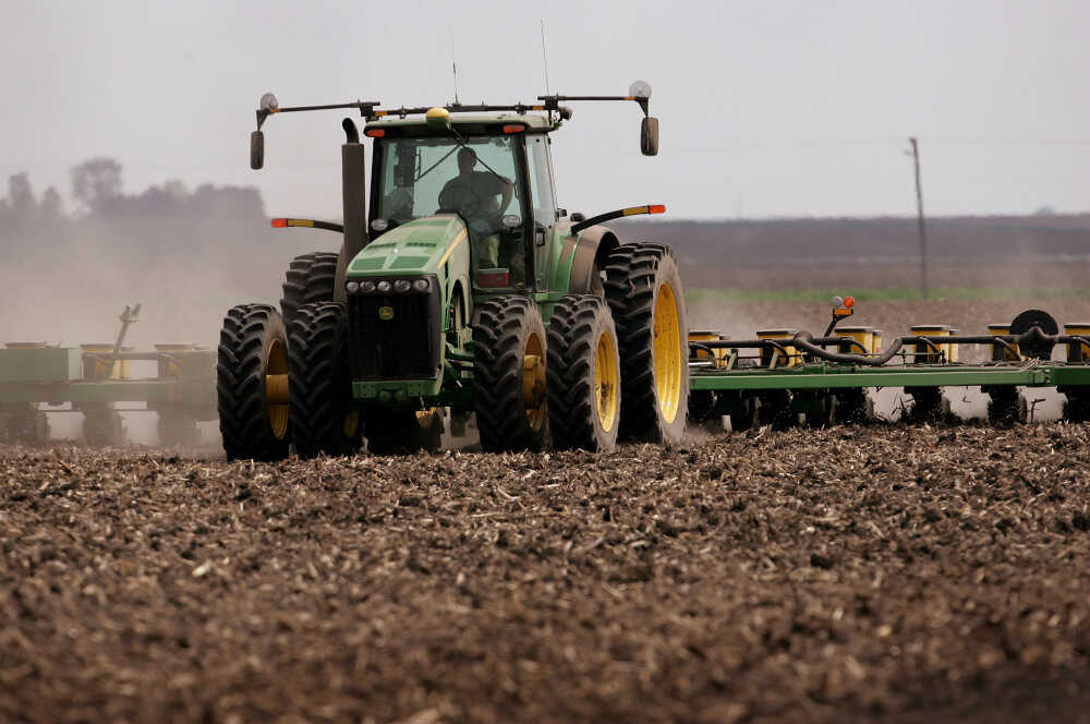 A green tractor that's planting corn moves across a brown dirt field in 2007 near Rochelle, Illinois.