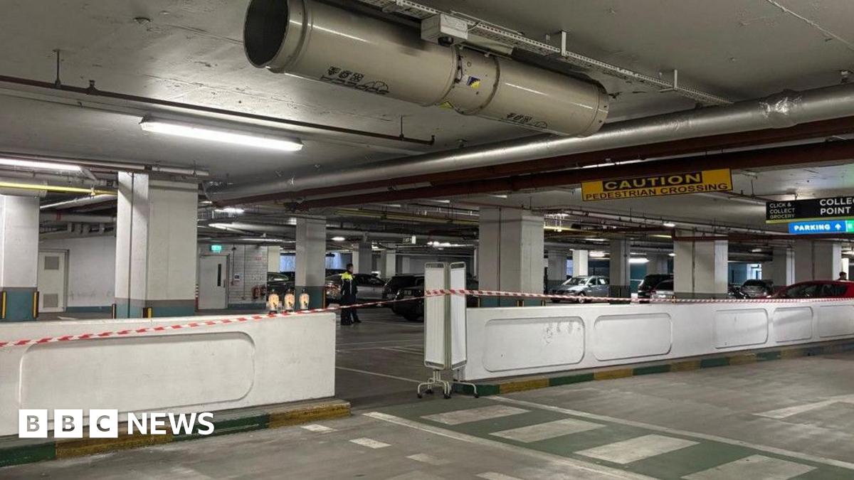 Scene of incident at Charlestown Shopping Centre underground car park in Finglas. There is red and white tape in the foreground as well as white walls. There is a yellow and black sign saying caution near the roof.