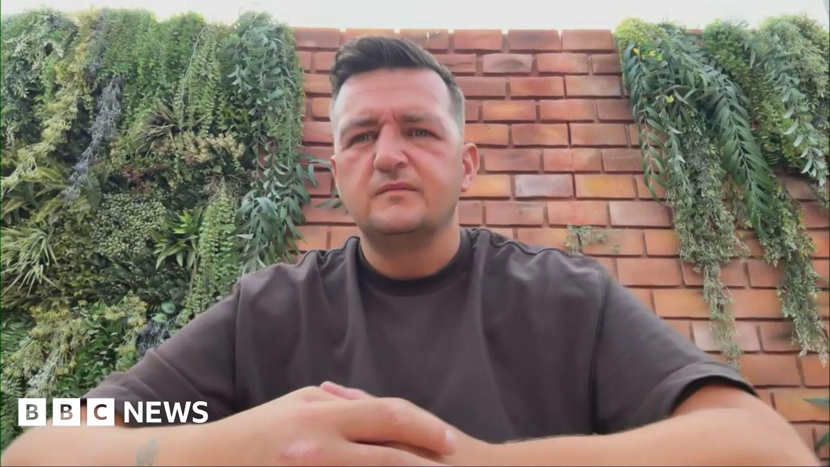 Gary Goldie looking right at the camera. He is wearing a brown T-shirt and is sitting in front of a brick wall.