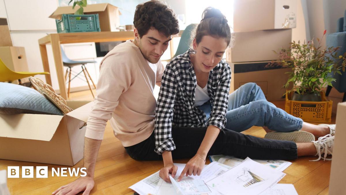 Young couple sit on the floor surrounded by boxes and paperwork.