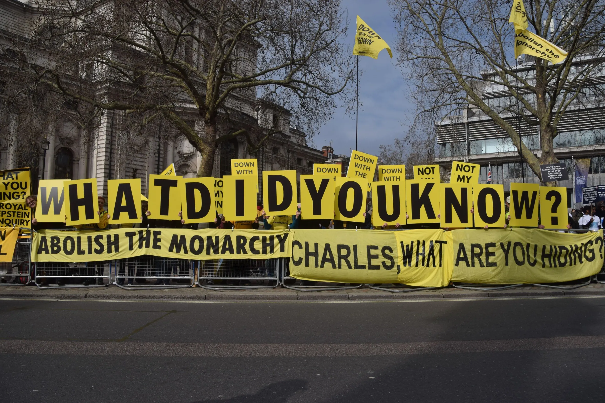 Anti-monarchy activists hold signs spelling "WHAT DID YOU KNOW?" and a banner reading "ABOLISH THE MONARCHY CHARLES, WHAT ARE YOU HIDING?"