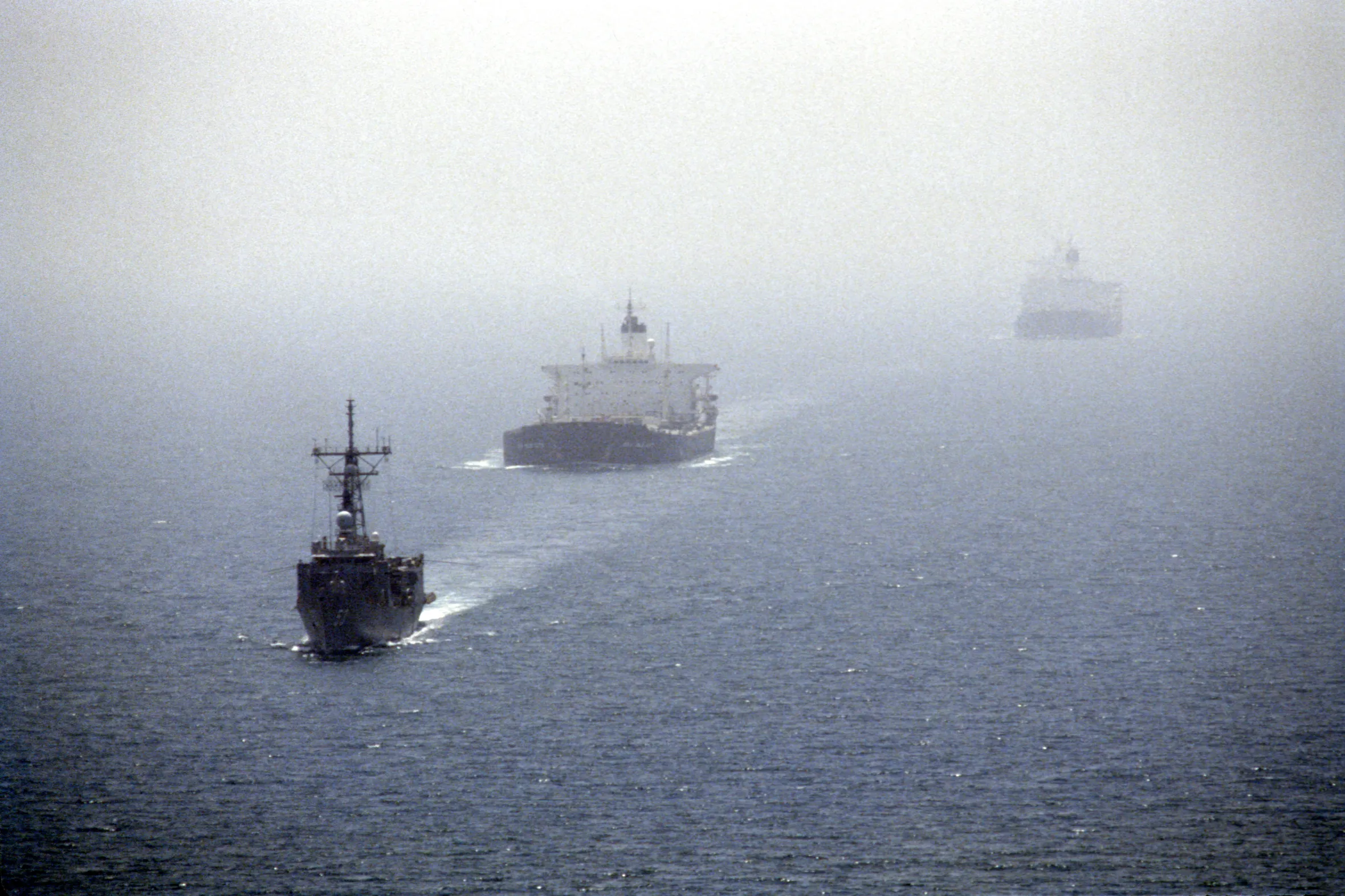 A US Navy destroyer escorts two reflagged Kuwaiti oil tankers through the Persian Gulf during Operation Earnest Will.