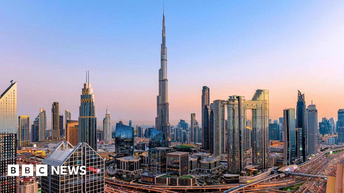 A large fire burns at an oil depot in Iran at night. Flames and thick plumes of dark smoke tower over the outline of a small building.