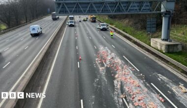 A motorway viewed from the bridge. Traffic officers have closed some of the lanes and a load of offal can be seen spread across several carriageways.