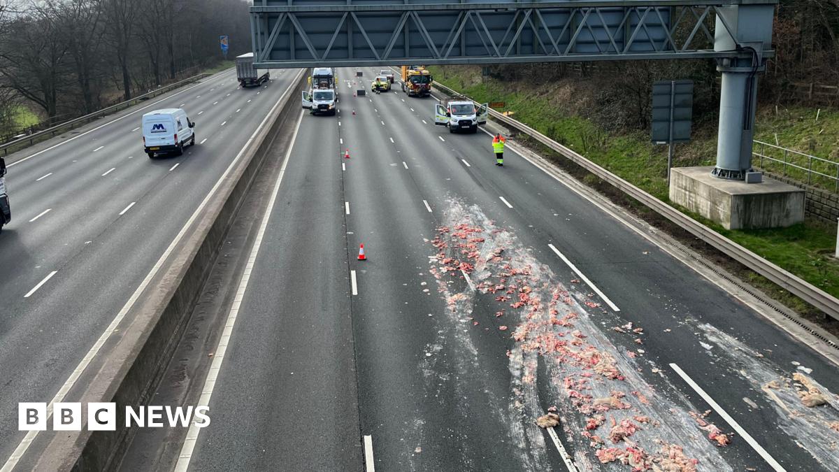 A motorway viewed from the bridge. Traffic officers have closed some of the lanes and a load of offal can be seen spread across several carriageways.