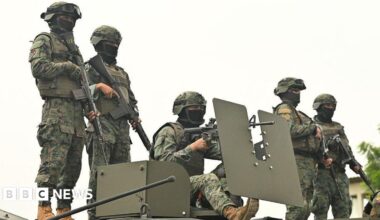 Five Ecuadorean soldiers stand atop an armoured vehicle at a command post in Guayas province. They are wearing camouflage uniforms, helmets and their faces are partly covered by black balaclavas. They are all heavily armed.