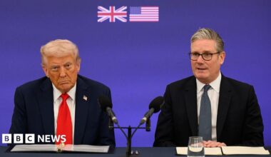 Donald Trump speaks with the media aboard Air Force One during a flight. He is wearing a black suit and red tie